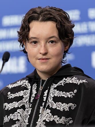 Bella Ramsey posing in a patterned dark jacket.